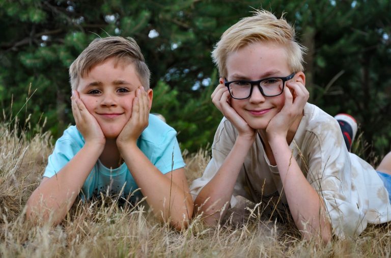 Portret van 2 broers Twee jongens liggen in het gras met hun handen onder hun kin en lachen.